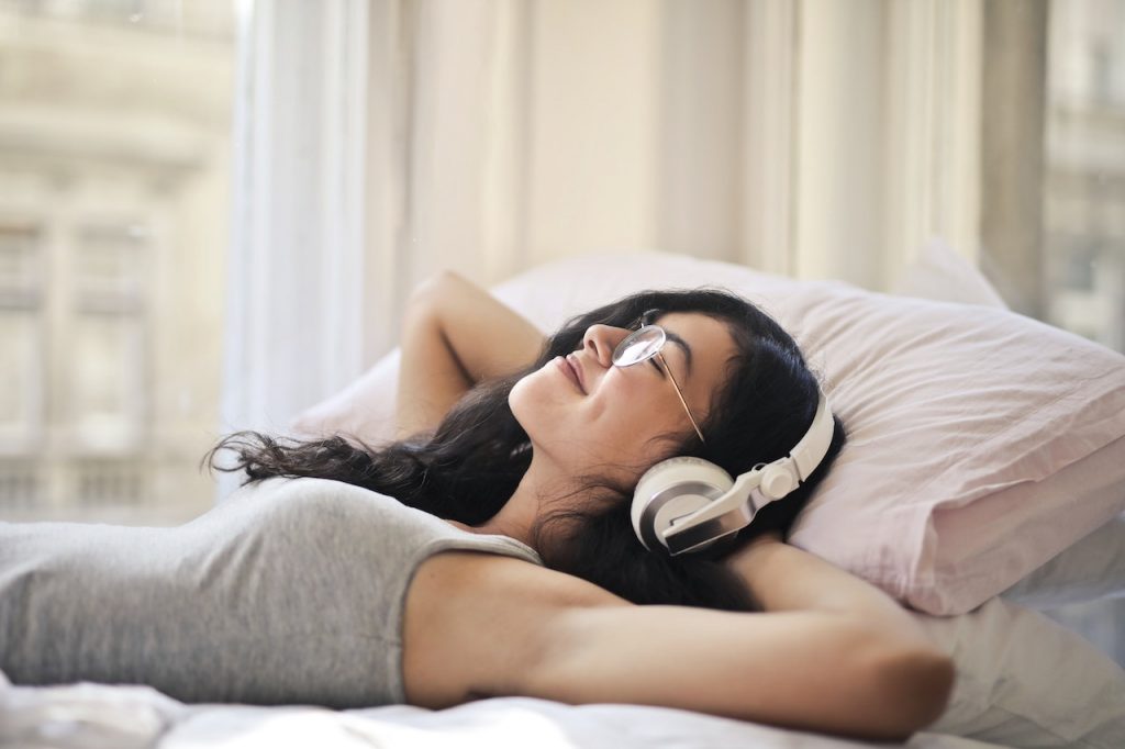 Una mujer está acostada en la cama escuchando música contemplativa.
