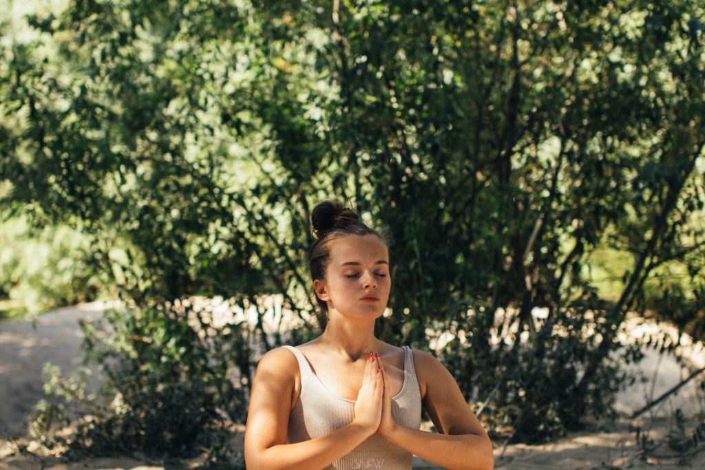 Una joven practica yoga en la arena durante un retiro online con música del Ángelus.