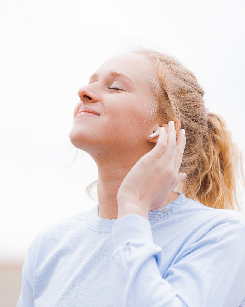 Una mujer vestida con una camiseta azul y auriculares escucha música en oración.